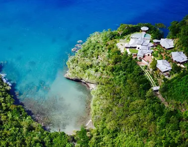 A view of the ocean from above shows a beach, houses and trees.